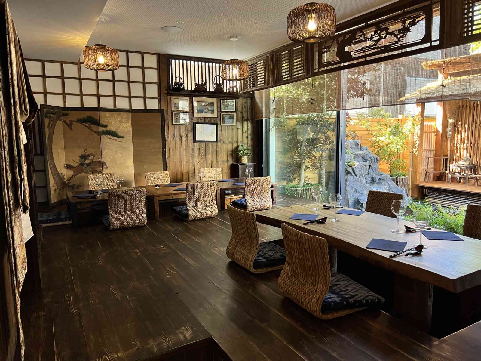 The namura dining room with low wooden tables, woven seats, a folding screen with a pine painting and a view onto the stone garden